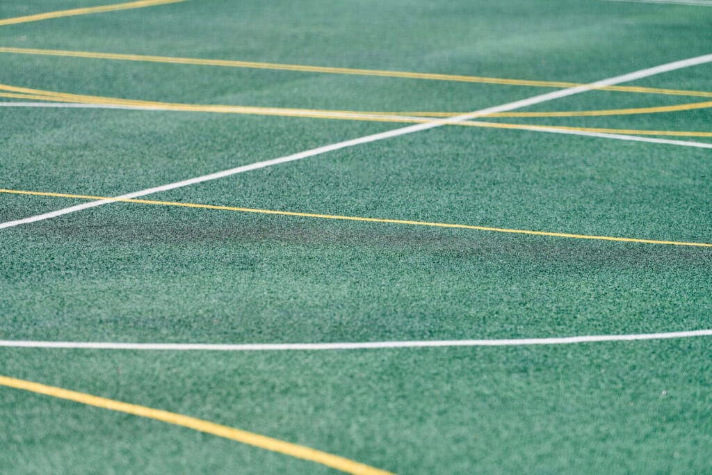 White and yellow line markings painted on green artificial grass sports pitch surface