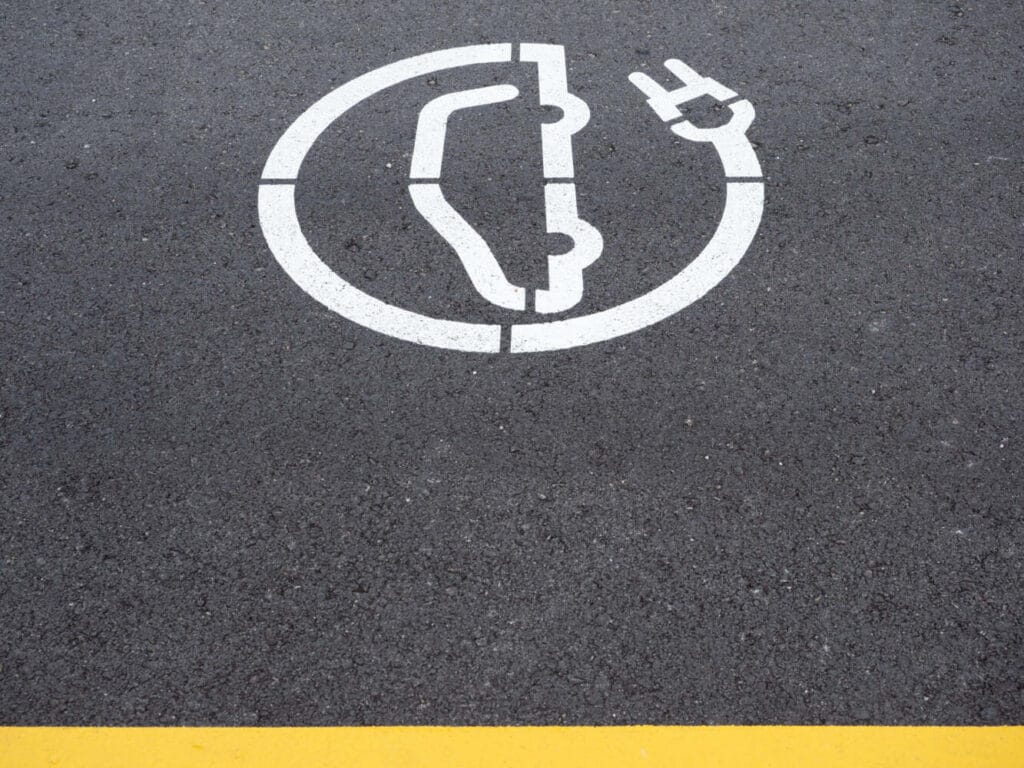 White electric vehicle charger symbol road marking painted on dark asphalt parking surface