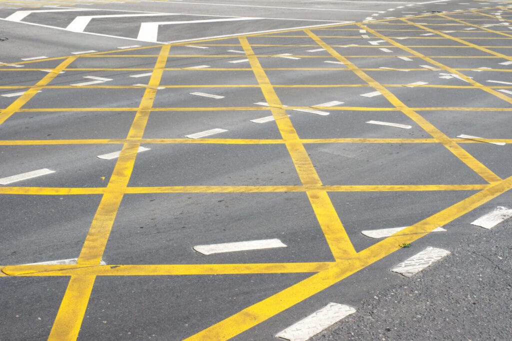 Yellow box junction markings at road intersection with white reflective cat's eye studs